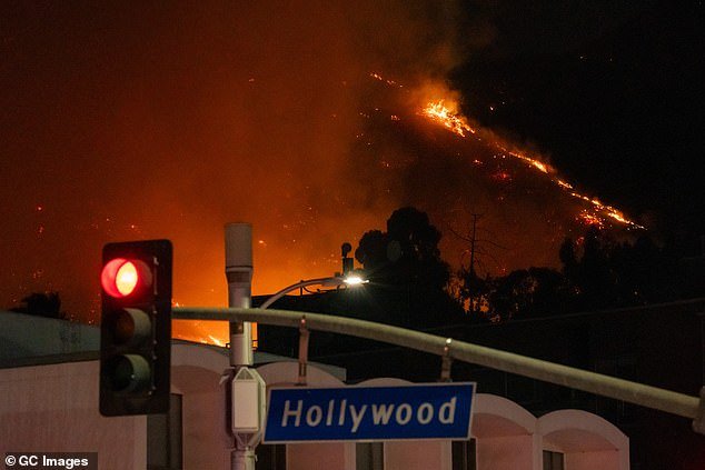 The death toll of the historic infernos have now reached five, as heroic firefighters still battle hellish conditions on the front lines of at least five different fires; Flames are seen on the hillsides above Hollywood Blvd on Wednesday