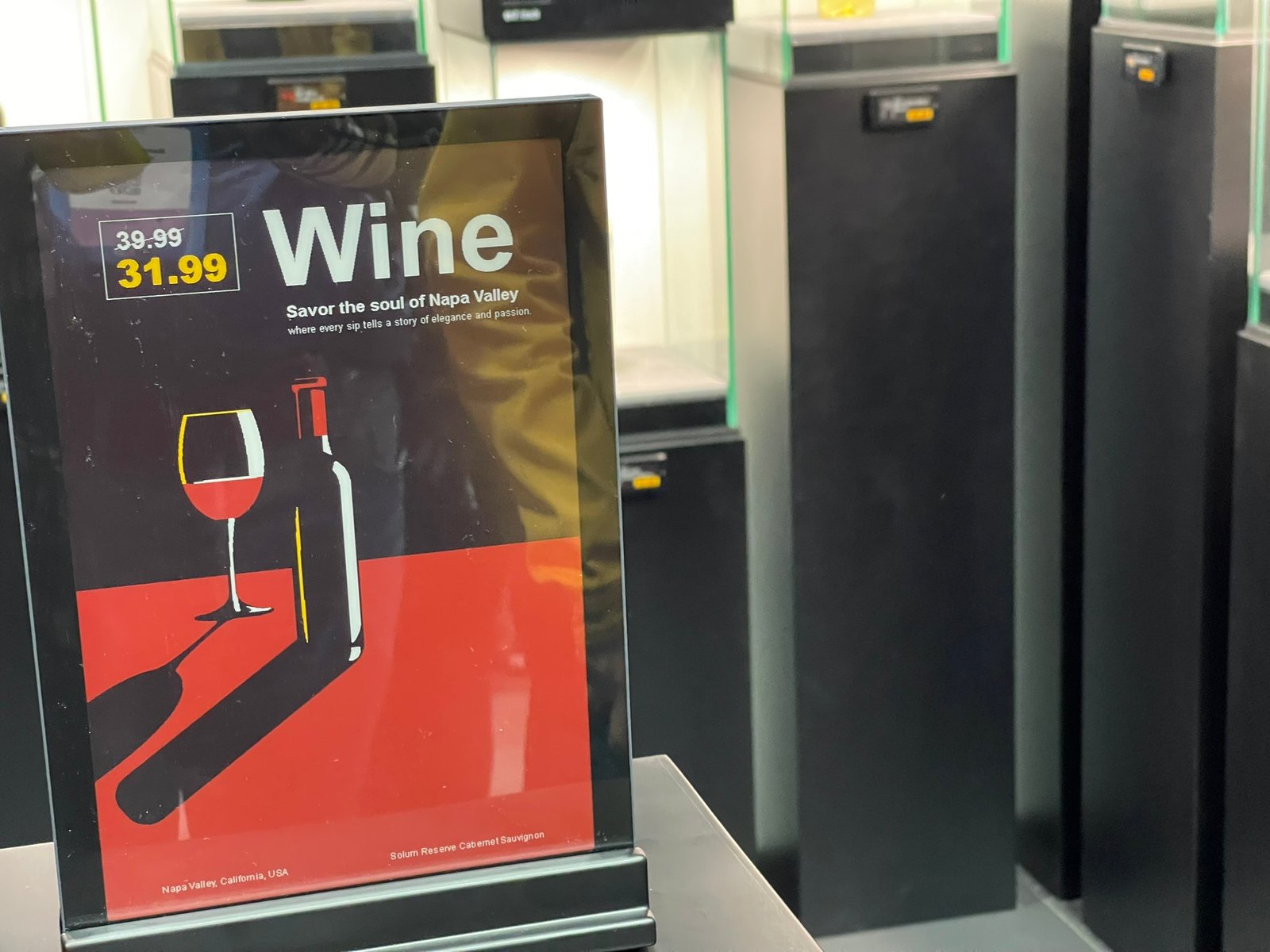 A large, vertical Solum e-ink display shows a pricing advertisement for wine.