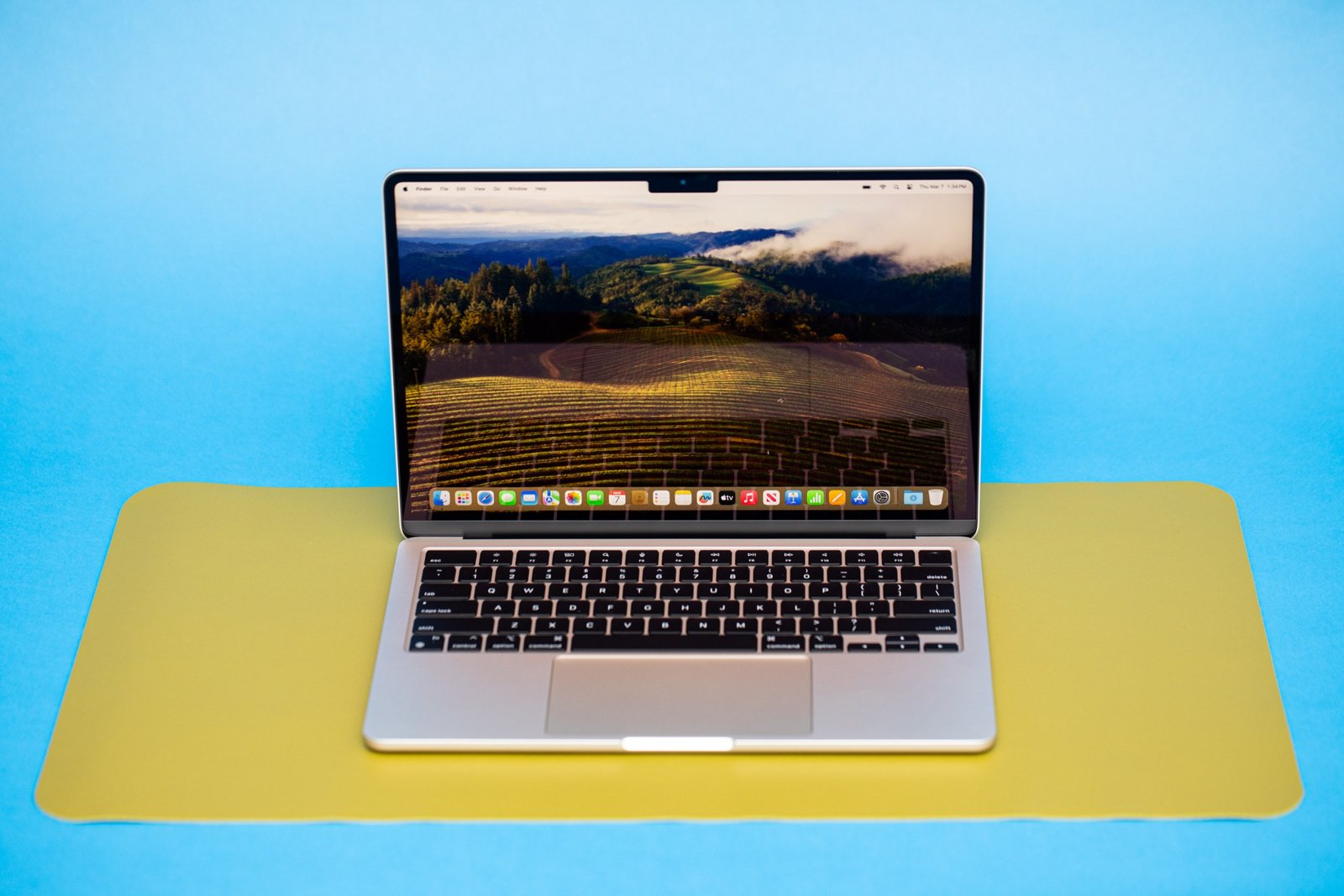 An open and powered on laptop against a blue background sitting on top of a bright yellow mat.